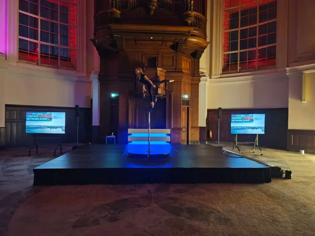 Podium zwart met rok eromheen. En een DJ booth met blauwe verlichting.